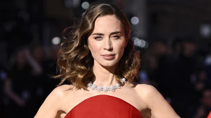 Emily Blunt mit einem roten Kleid stemmt die Hände in die Hüfte.