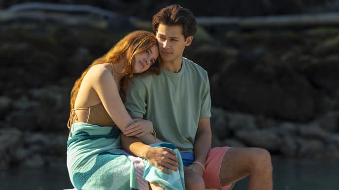 Eine junge Frau mit langen rötlichen Haaren lehnt ihren Kopf auf die Schulter eines jungen Mannes.