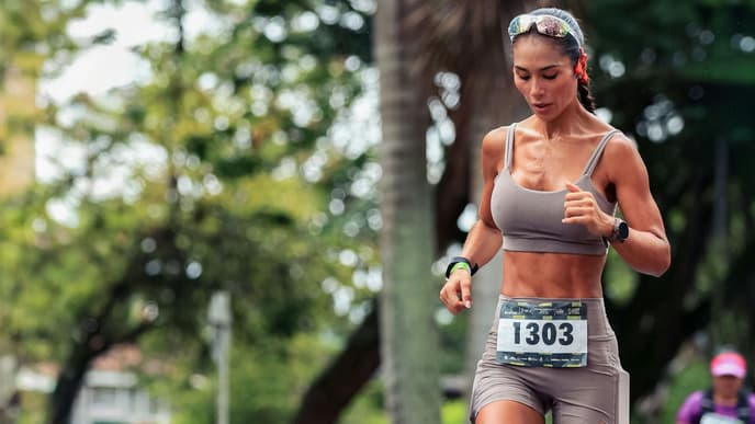 Eine Frau in einem beigefarbenen Sportoutfit mit Startnummer läuft auf der nassen Straße.