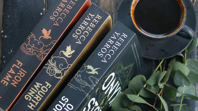 Drei Bücher liegen hochkant auf einem Tisch mit einer Tasse Kaffee und Eukalyptus-Sträuchern.