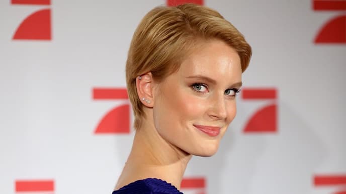 Kim Hnizdo mit kurzen Haaren und einem blauen Oberteil guckt über die Schulter in die Kamera.