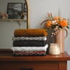 Gefaltete Wollpullover auf einer Holkommode neben einer Kerze und einer Blumenvase