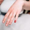 Hand mit natürlichen Nägeln und rotem Nagellack auf dem kleinen Finger