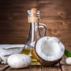 Kokosöl Haare: Ölflasche steht neben einer halben Kokosnuss und einer Kerze auf einem Tisch