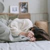 Frau im Bett mit Händen vor Gesicht 