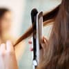 Frau glättet sich die Haare mit Dampfglätteisen