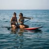 Zwei Frauen sitzen auf Surfboard im Meer