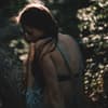 Frau im Wald guckt traurig zur Seite 
