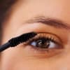 Frau trägt Mascara auf mit braunen Augen