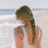 Frau mit geflochtenen Haaren sitzt am Strand
