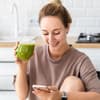 Frau mit grünem Saft schaut auf Handy