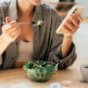 Frau isst Salat mit Smartphone in der Hand