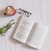 Buch liegt neben Brille und Kaffee