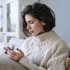 Frau mit kurzen braunen Haaren schaut traurig auf ihr Smartphone