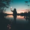 Frau am See hält eine Glühbirne mit einer Lichterkette in der Hand.