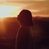 Frau mit kurzen Haaren steht vor einem Sonnenuntergang