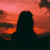 Silhouette einer Frau mit langen Haaren vor einem orange-rosafarbenen Himmel