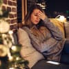 Gestresste Frau sitzt auf dem Sofa, neben ihr ein geschmückter Tannenbaum