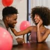 Mann und Frau sitzen am Tisch mit Luftballons und lachen