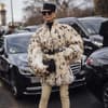 Frau trägt auf Paris Fashion Week Fake Fur Mantel XXL Hut und Sonnenbrille plus beigefarbene Overknees