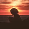 Frau sitzt beim Sonnenuntergang am Meer