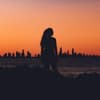Frau steht vor einer Skyline während des Sonnenuntergangs