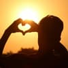 Person zeigt Herz vor Sonne