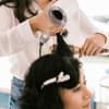 Friseurin stylt Haare der Kundin mit Föhn und Rundbürste