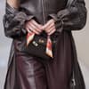Eine Frau trägt ein braunes Outfit und hält vorn ihre Tasche mit den Fingern fest.