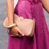 Eine Nahaufnahme einer Frau mit einem Kleid mit Lochmuster in Magenta und einer hellbraunen Clutch in der Hand mit goldenen Armreifen.