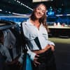 Eleni Frommann begleitet sechs Wochen lang die Fußball-Weltmeisterschaft in den USA. Eine junge Frau in einem weißen Sportoberteil lehnt gegen ein Auto und lacht in die Kamera.