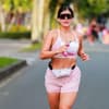 Ein Halbmarathon bei über 30 Grad ist mental und körperlich eine große Herausforderung. Eine junge Frau mit einer Sonnenbrille, Sportkleidung und einer kleinen Wasserflasche am Laufen auf der Straße.