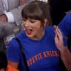 Taylor Swift sorgte mit ihrem Graphic Shirt beim Knicks Spiel für Aufsehen. Taylor Swift mit einem blauen Shirt schreit euphorisch und schaut zur Seite nach links.