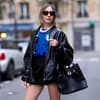 Eine Frau trägt einen schwarzen kurzen Rock, ein Italien Trikot, eine schwarze Lederjacke und eine Sonnenbrille plus Tasche.