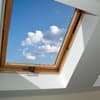 Im Sommer kann eine Dachgeschosswohnung zum Verhängnis werden. Dachgeschoss Fenster aus Holz mit Blick auf den blauen Himmel mit Wolken.