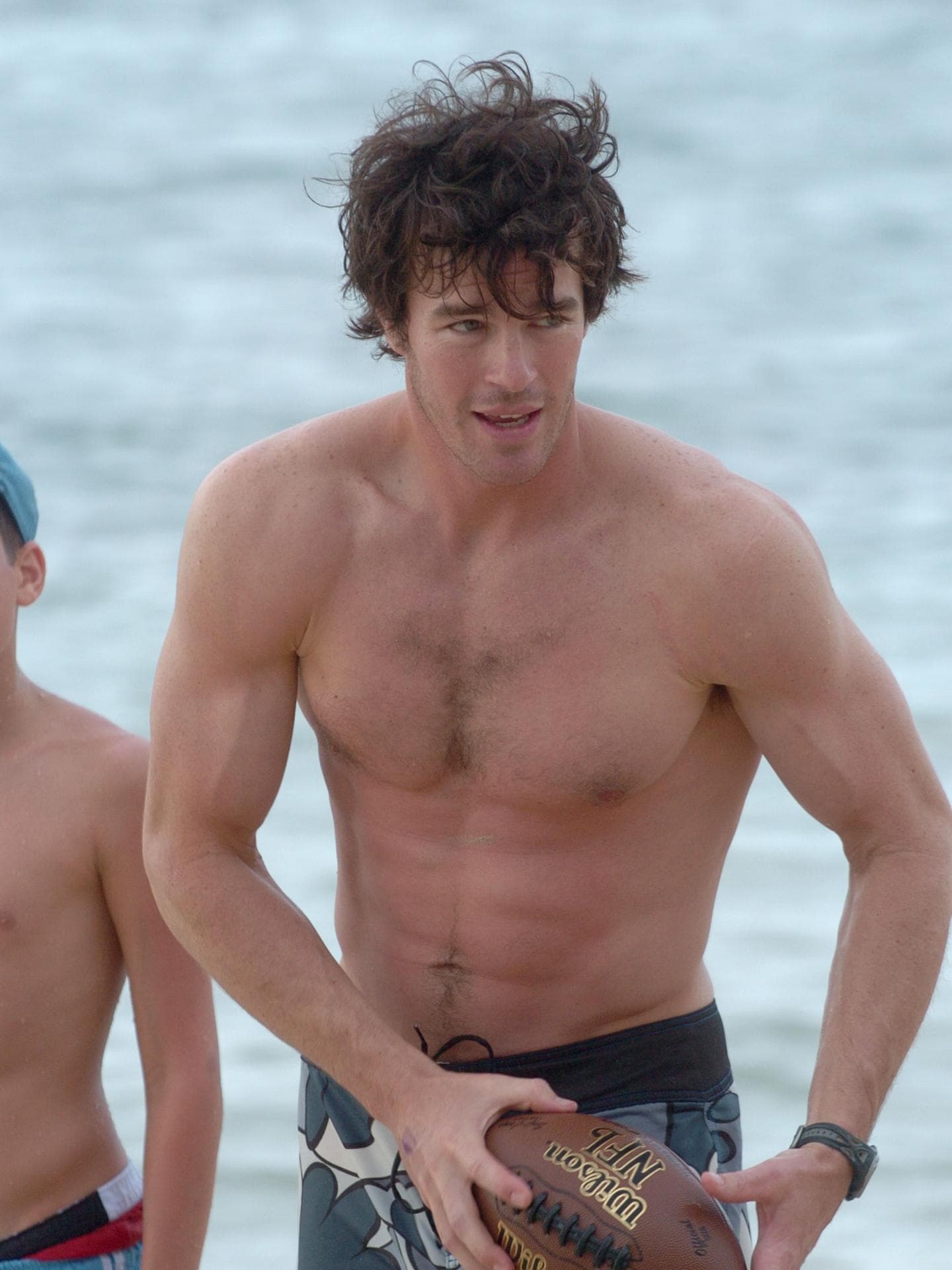 Ryan Sutter oberkörperfrei mit Football am Strand