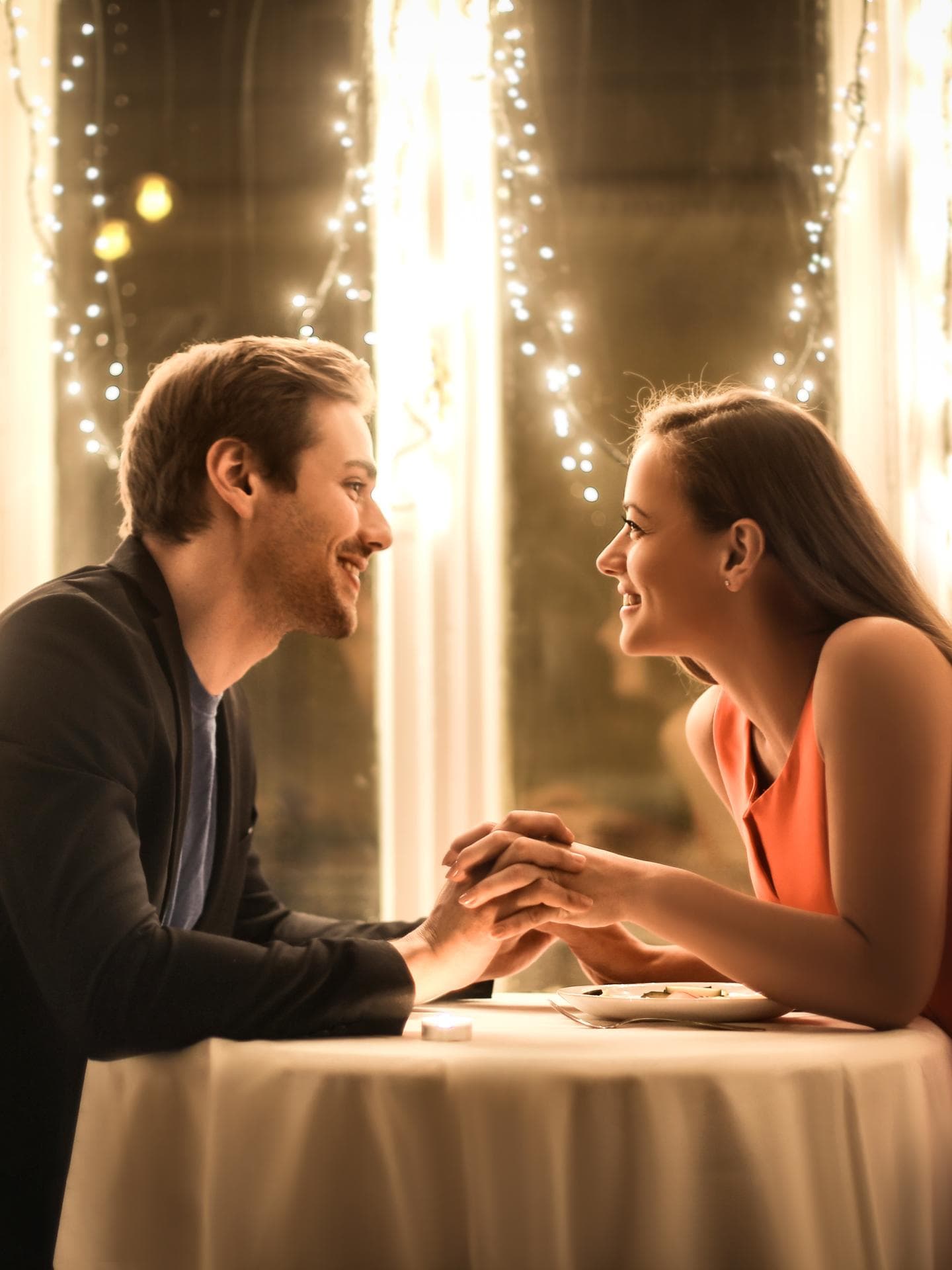 Valentinstag Date: Die besten Ideen für Verliebte Valentinstag Date: Mann und Frau sitzen an einem Tisch der mit Lichterketten geschmückt ist