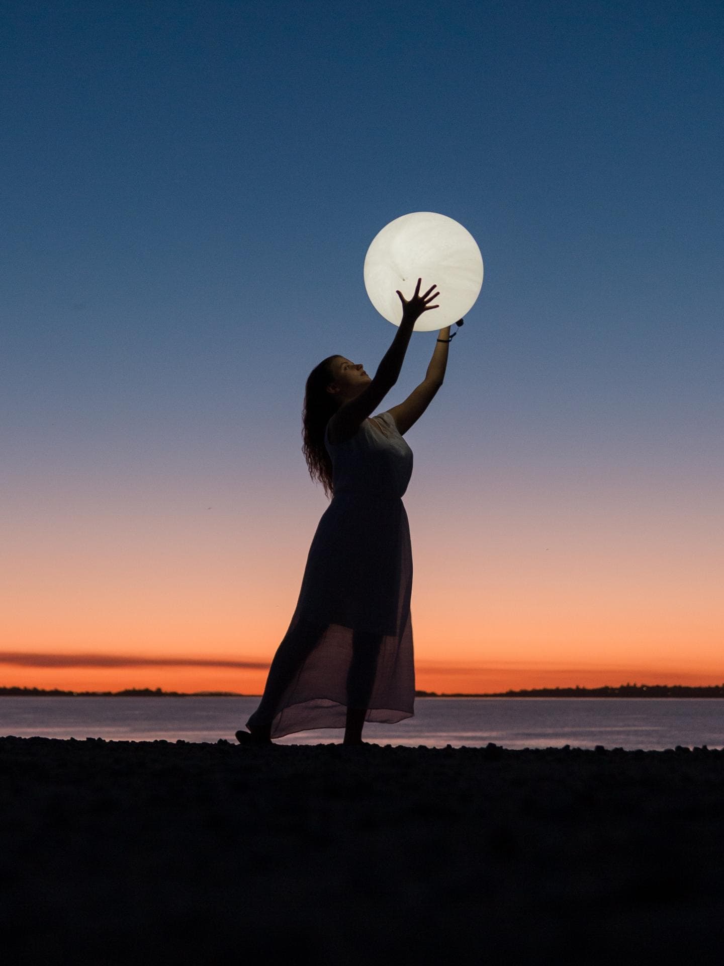Horoskop: Frau hält einen Vollmond in der Hand am Strand