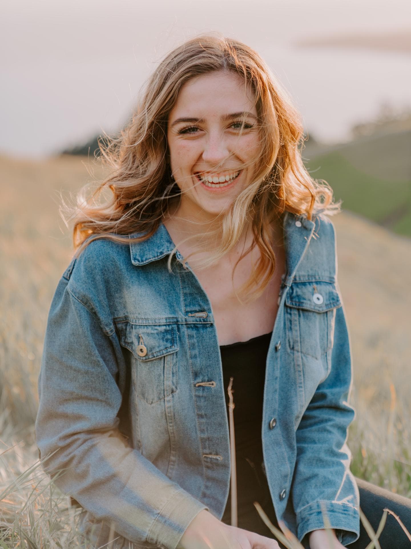 Horoskop: Frau lacht im Feld mit Jeansjacke