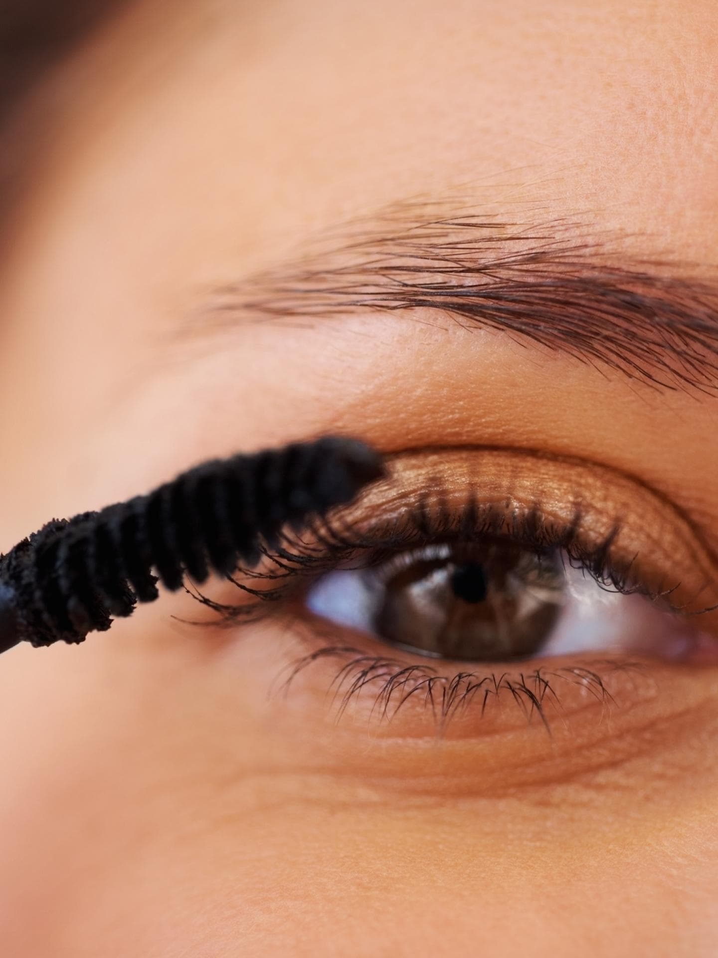 Frau trägt Mascara auf mit braunen Augen