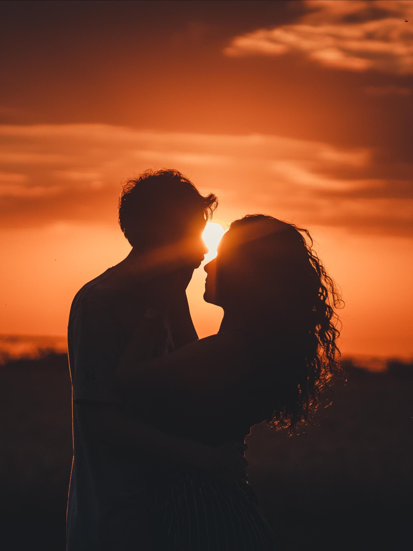 Mann und Frau umarmen sich mit Sonnenuntergang im Hintergrund
