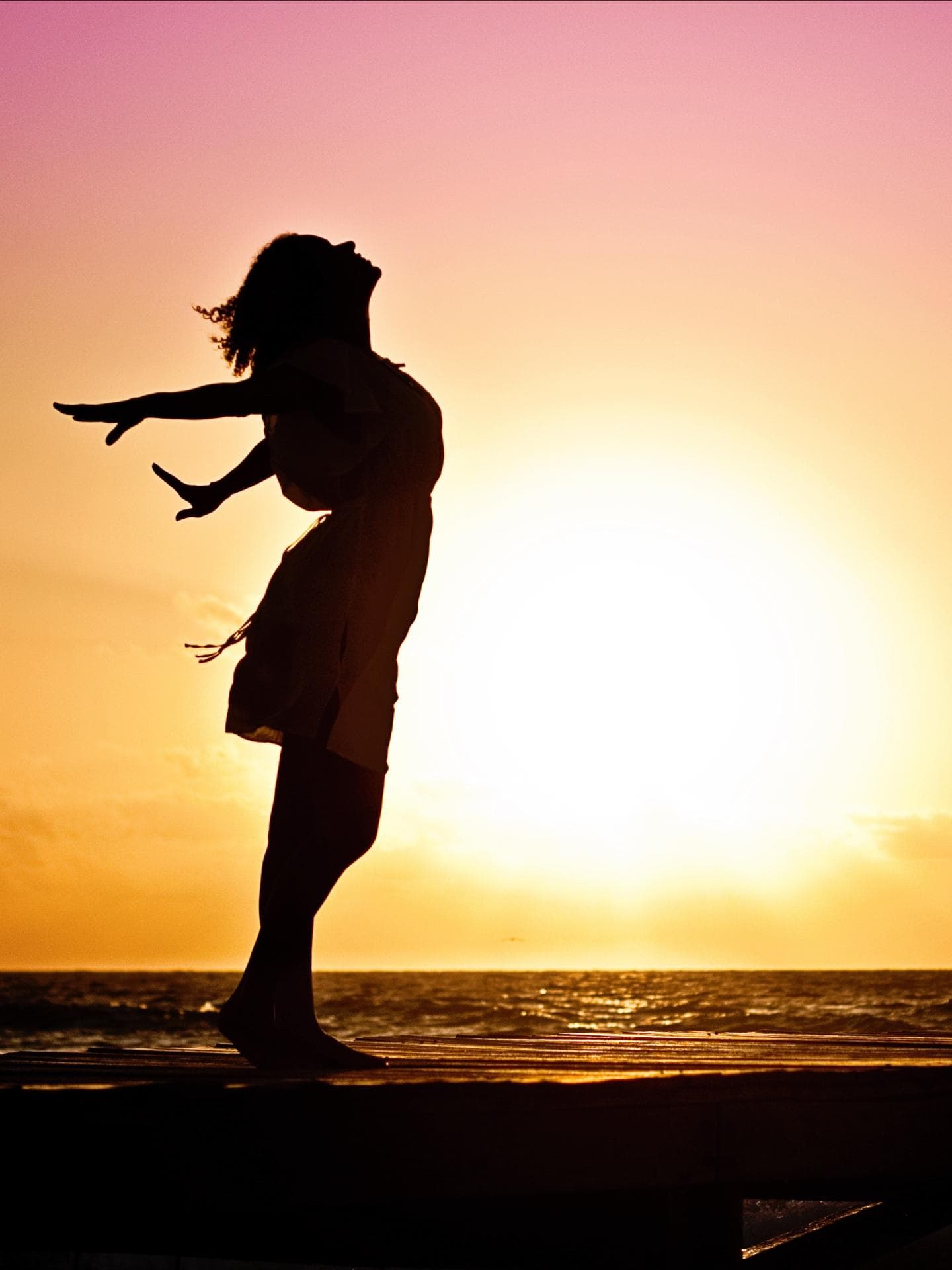 Silhouette einer Frau vor einem Sonnenaufgang, die die Arme nach hinten ausstreckt