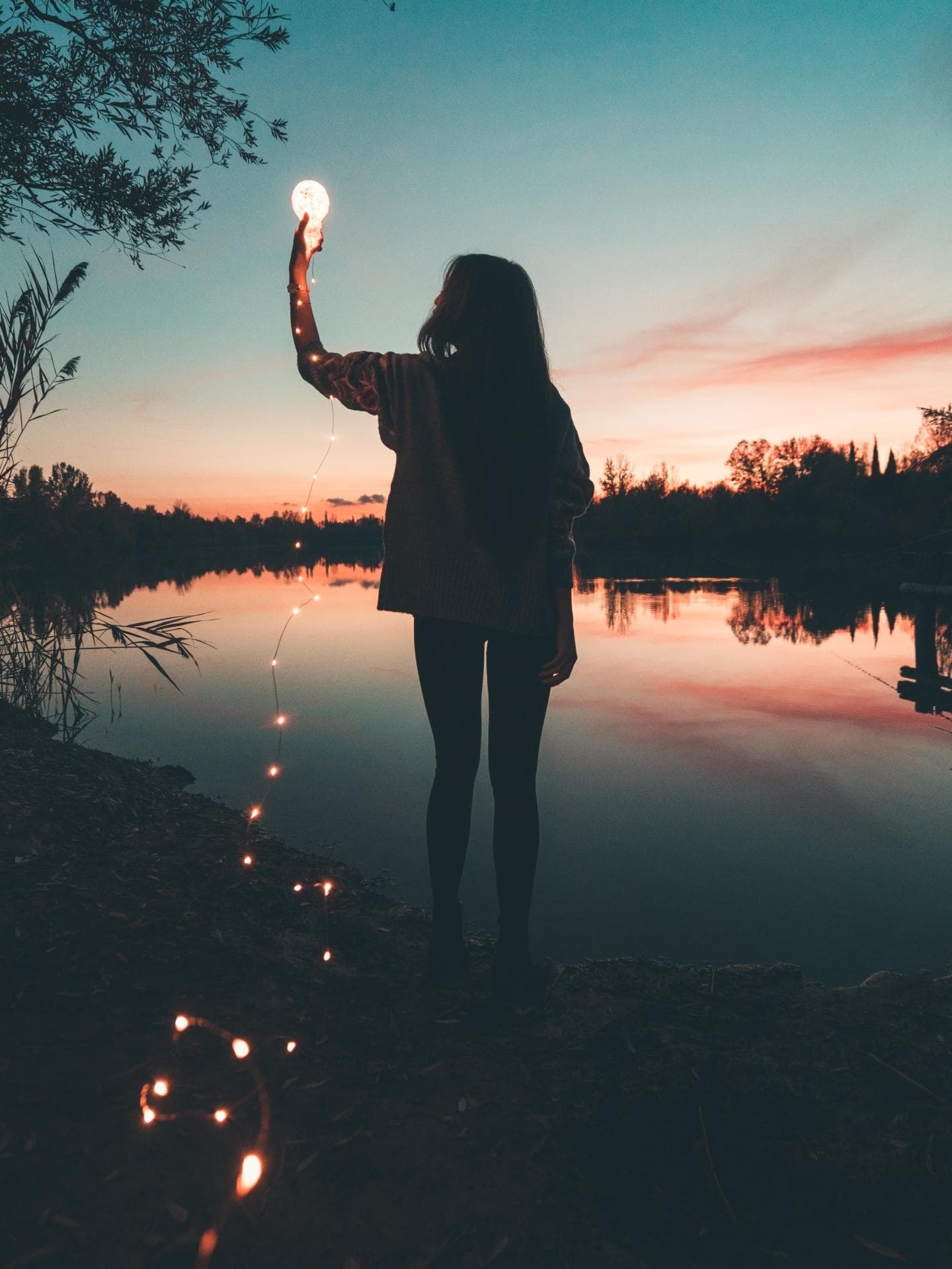Horoskop Wochenende Frau am See hält eine Glühbirne mit einer Lichterkette in der Hand.