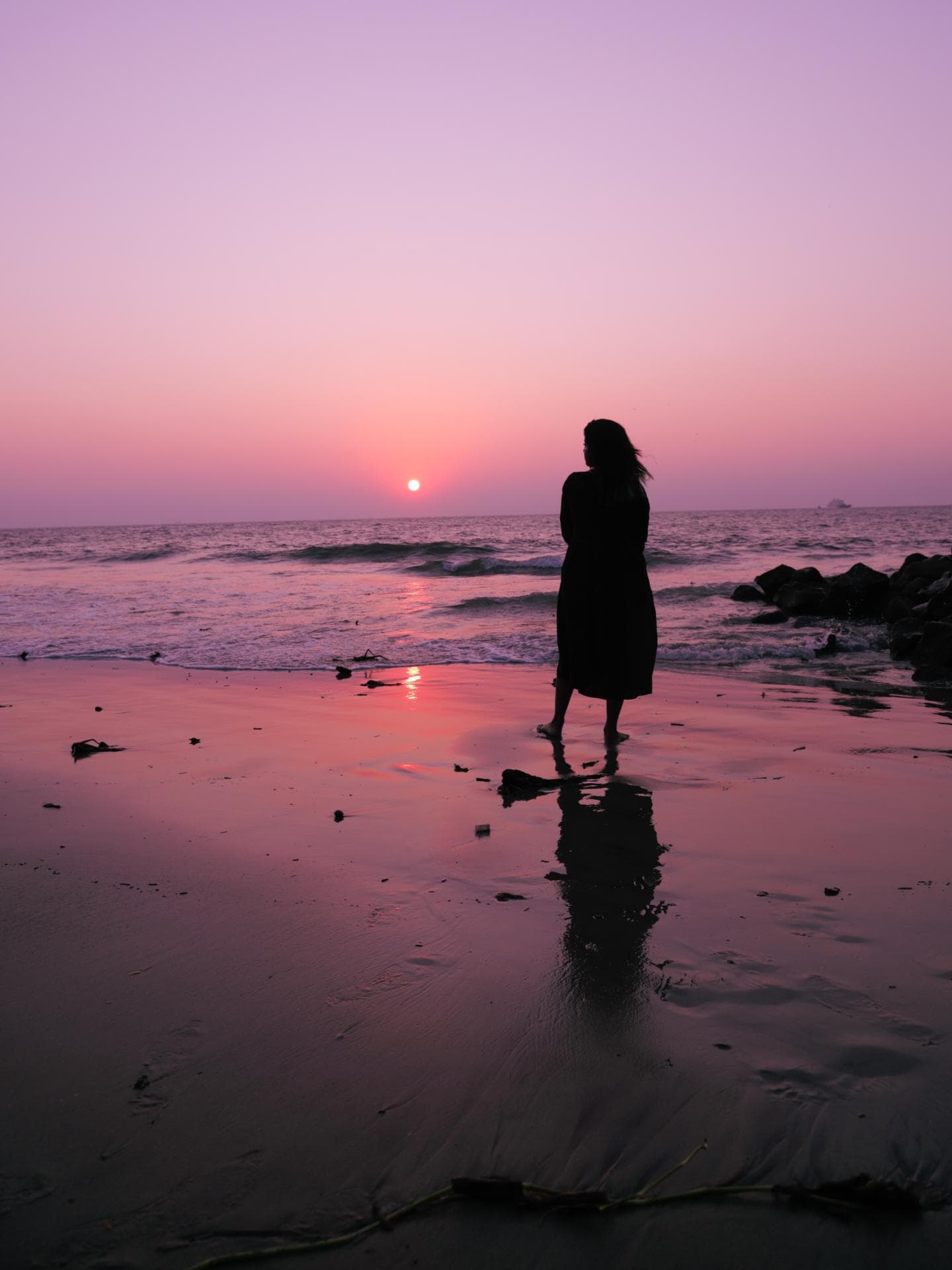 Frau steht am Strand und schaut den Himmel an