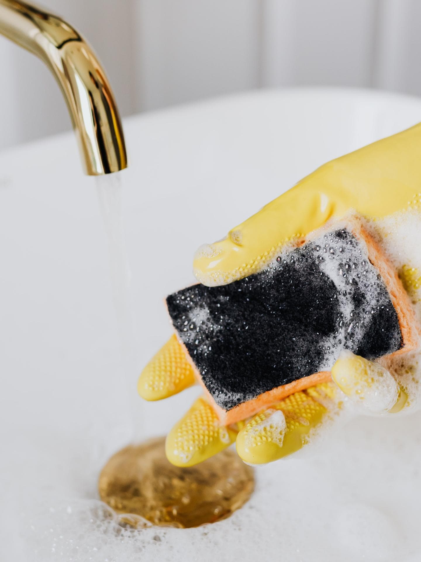Gelber Handschuh mit Schwamm im Waschbecken