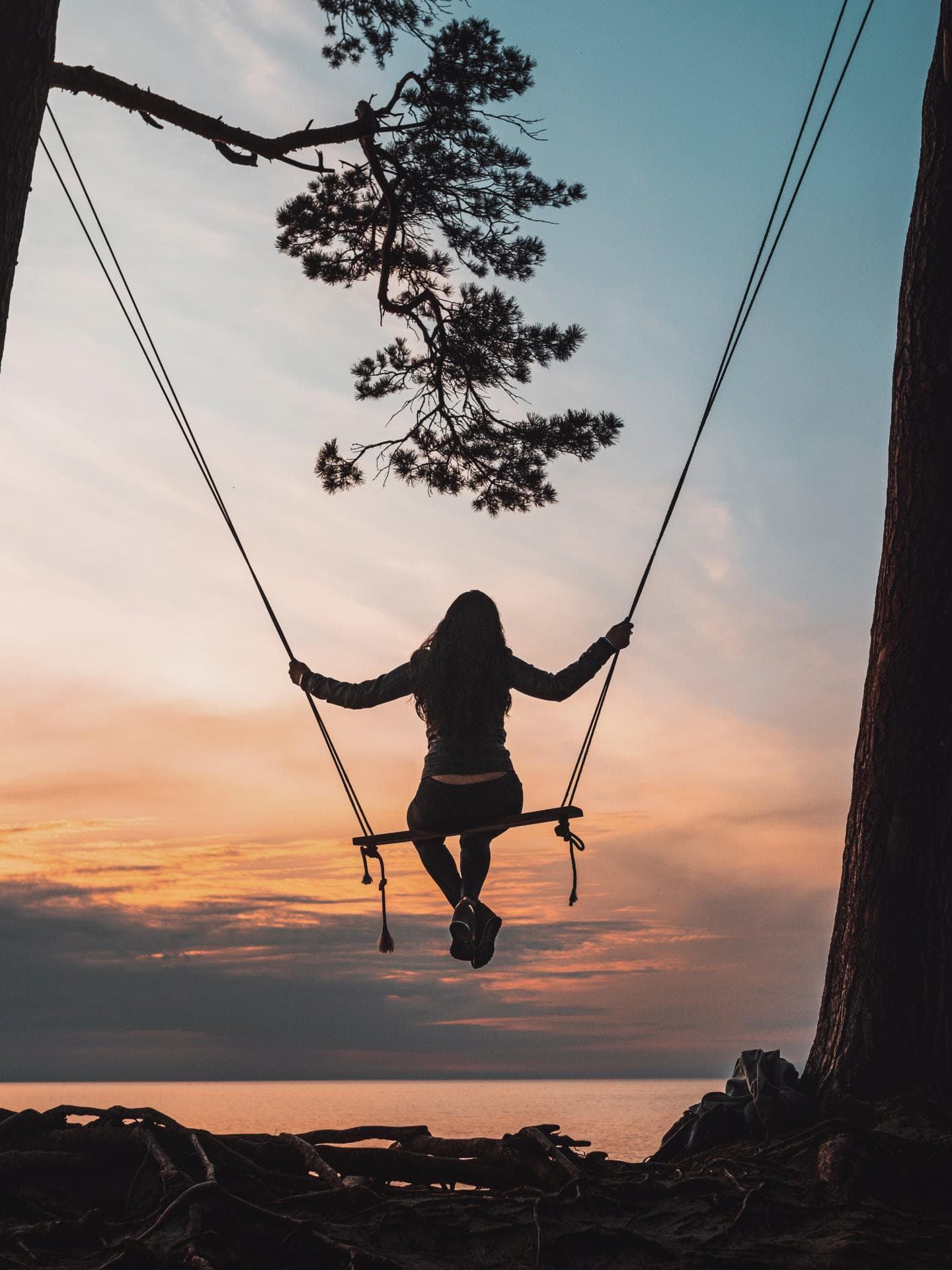 Frau auf einer Schaukel beim Sonnenaufgang