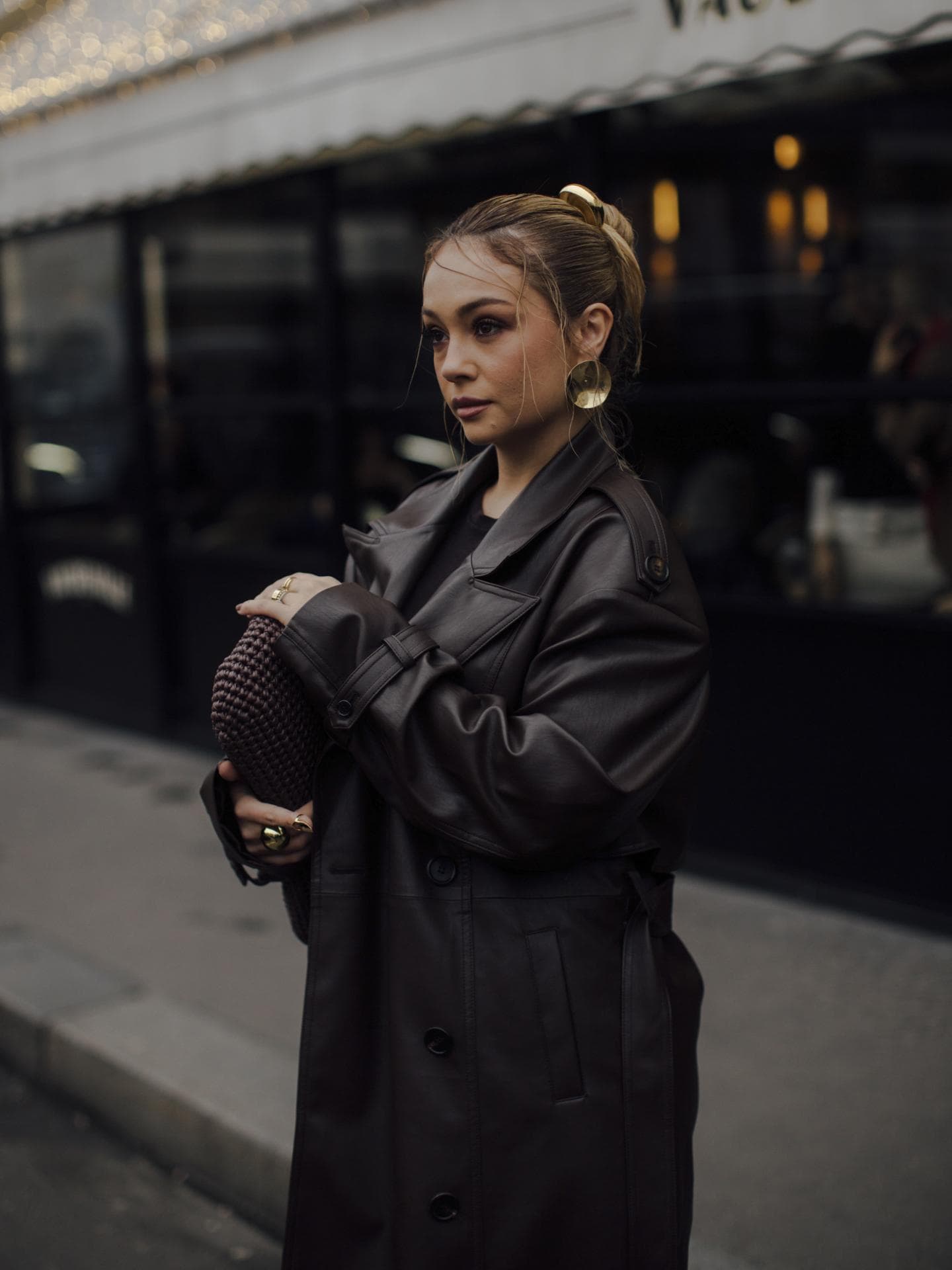 Frau trägt auf Paris Fashion Week braunen Ledermantel goldene Ohrringe und braune Tasche Frau trägt auf Paris Fashion Week braunen Ledermantel goldene Ohrringe und braune Tasche