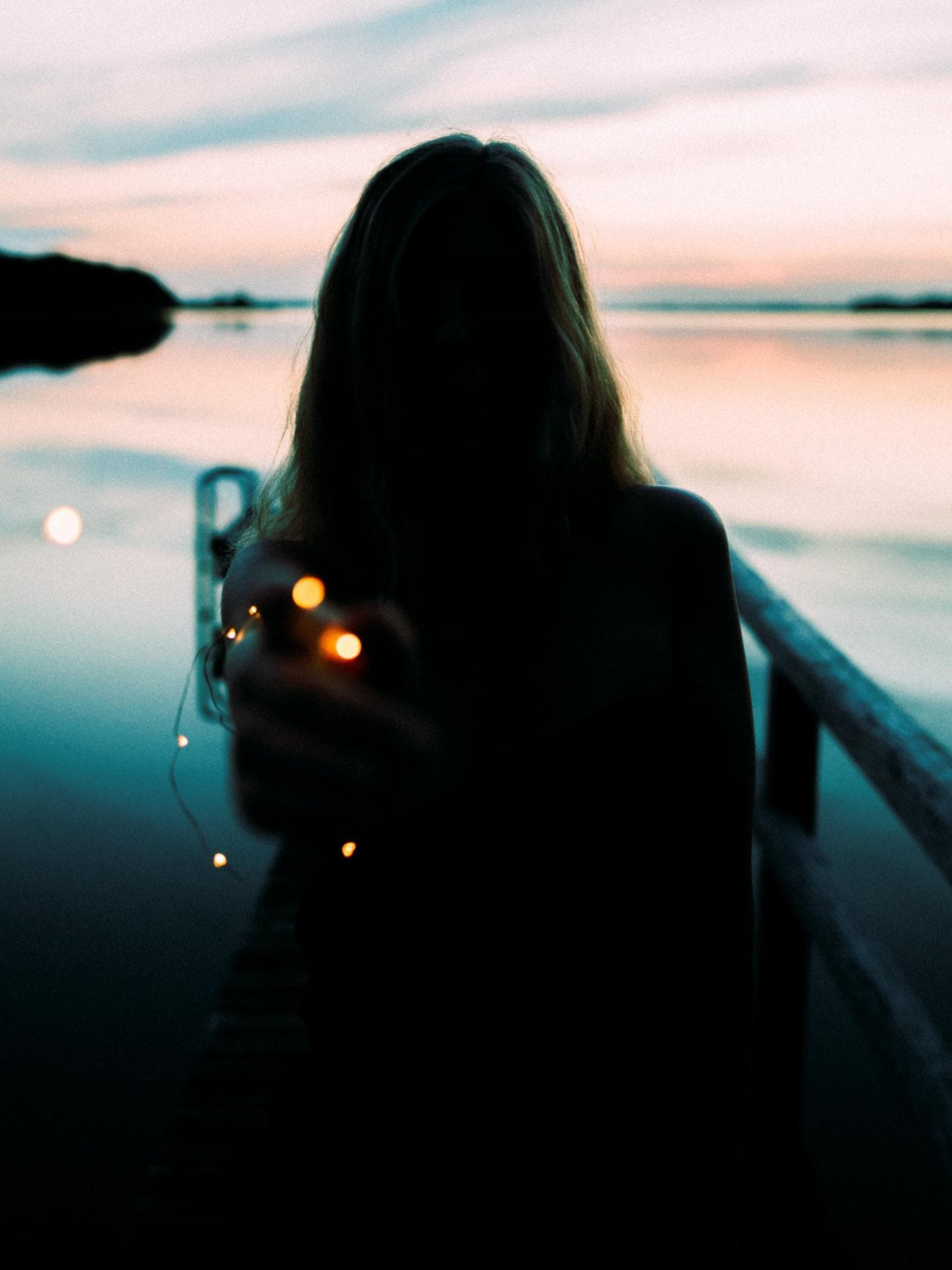 Frau steht am See mit einer Lichterkette