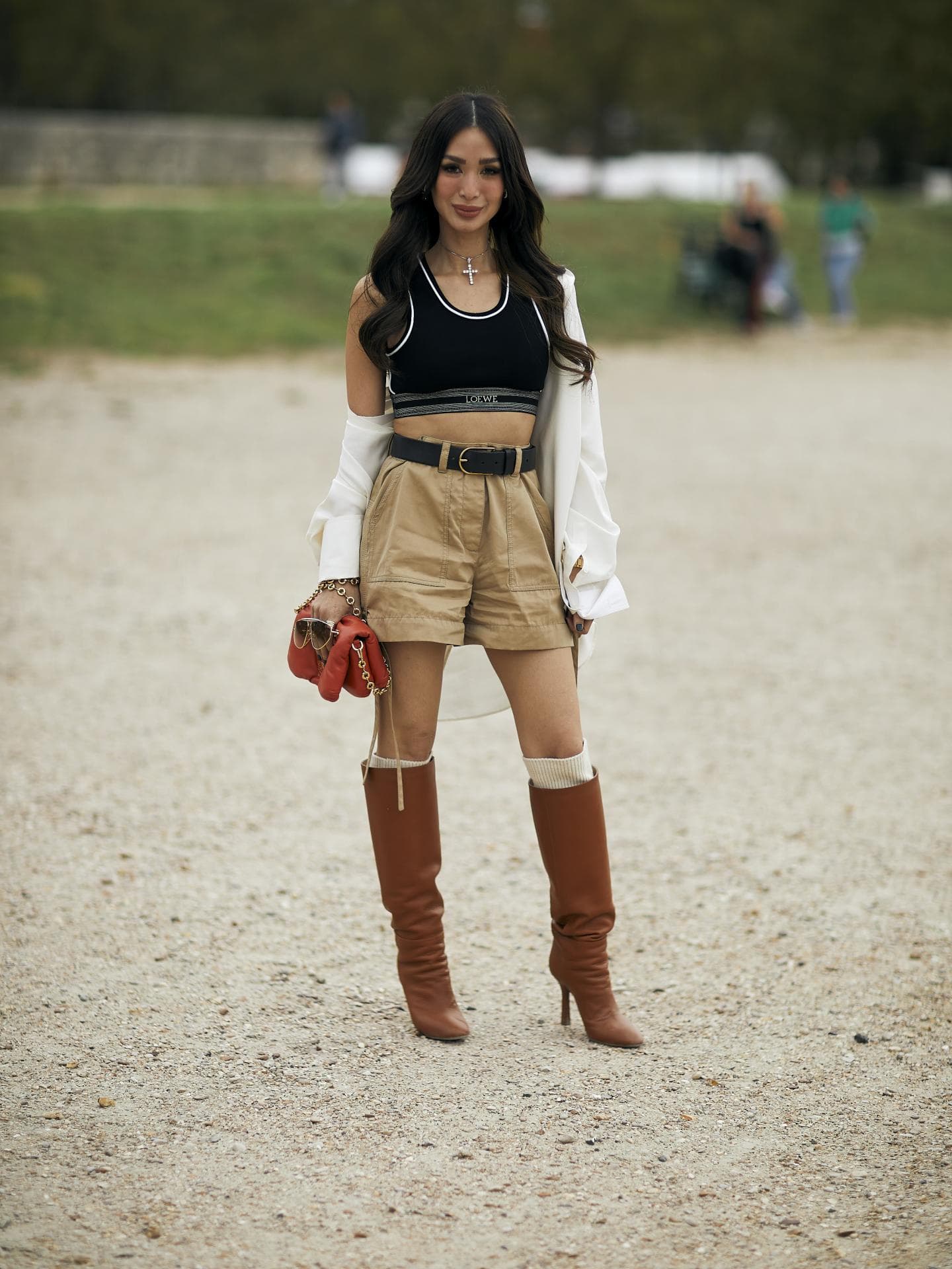 Frau trägt auf Paris Fashion Week beigefarbene Shorts mit weißem Hemd und Sport-BH sowie kniehohe Stiefel Frau trägt auf Paris Fashion Week beigefarbene Shorts mit weißem Hemd und Sport-BH sowie kniehohe Stiefel