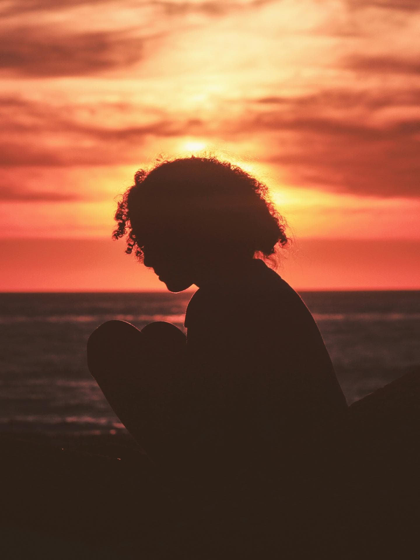 Frau sitzt beim Sonnenuntergang am Meer